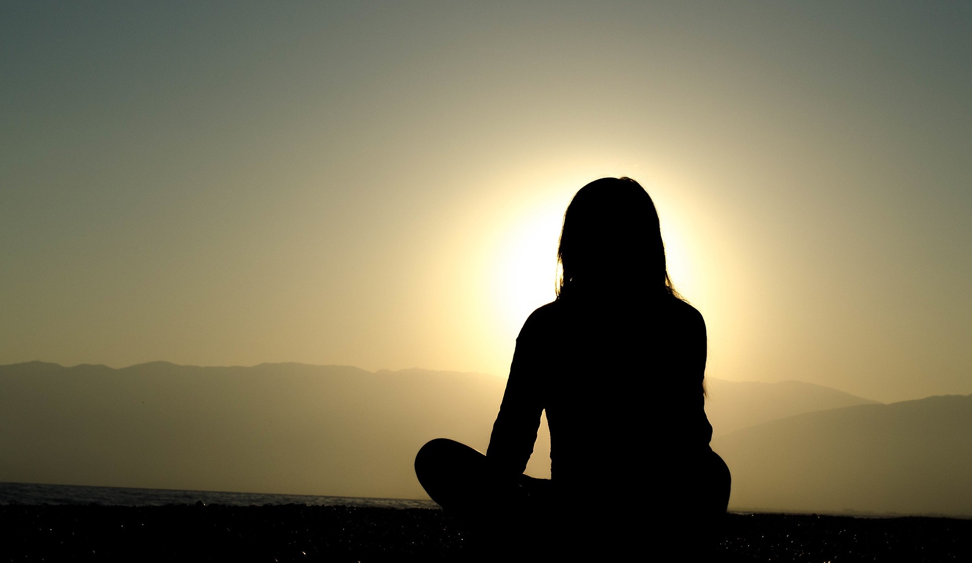 a women sits in meditation at sunset